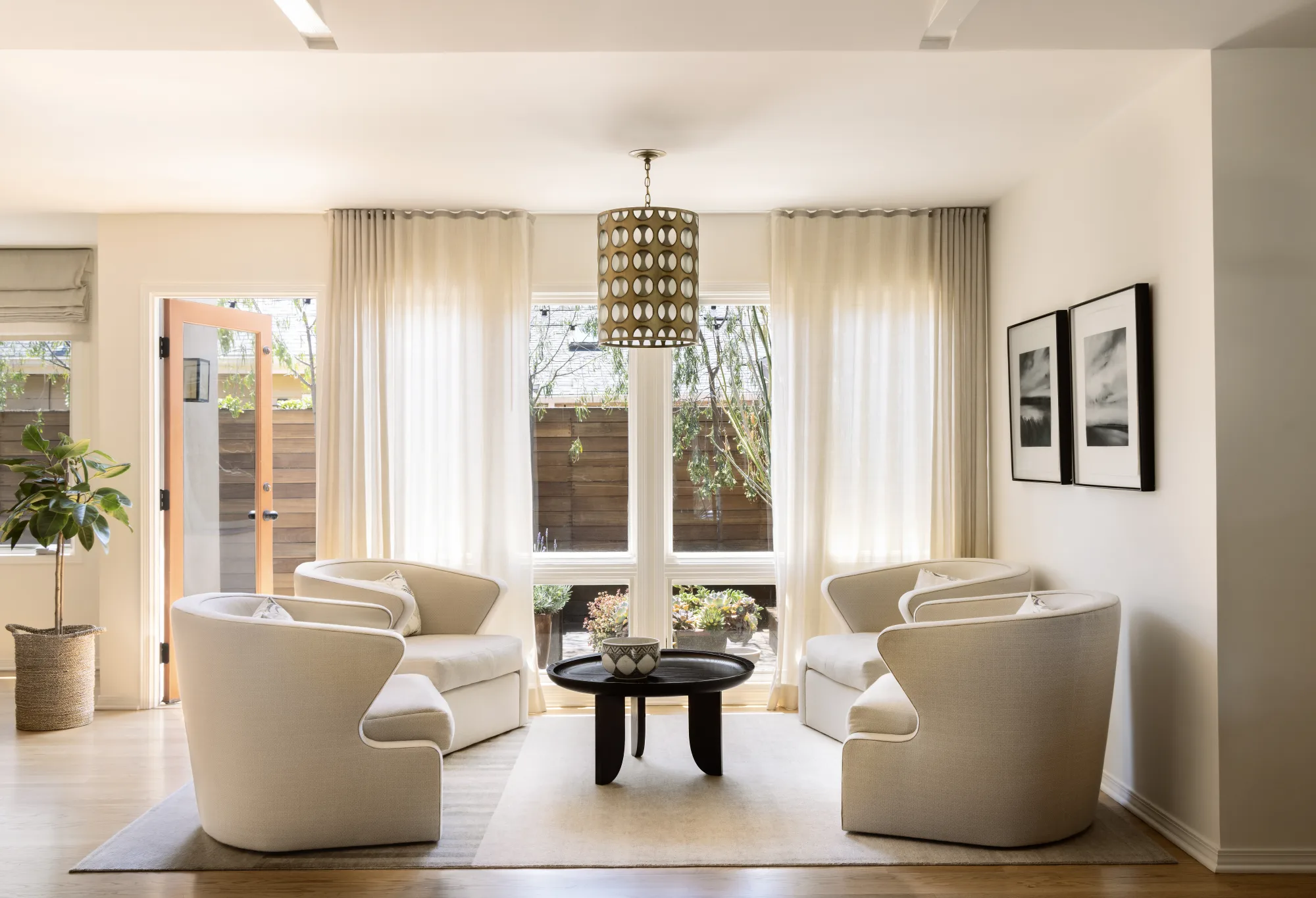Sitting area with four white swivel chairs around a black table beneath a woven pendant
